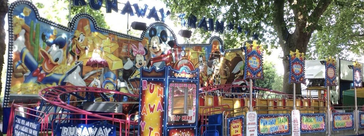 Runaway Train funfair ride set up under park trees with large cartoon character frontboard