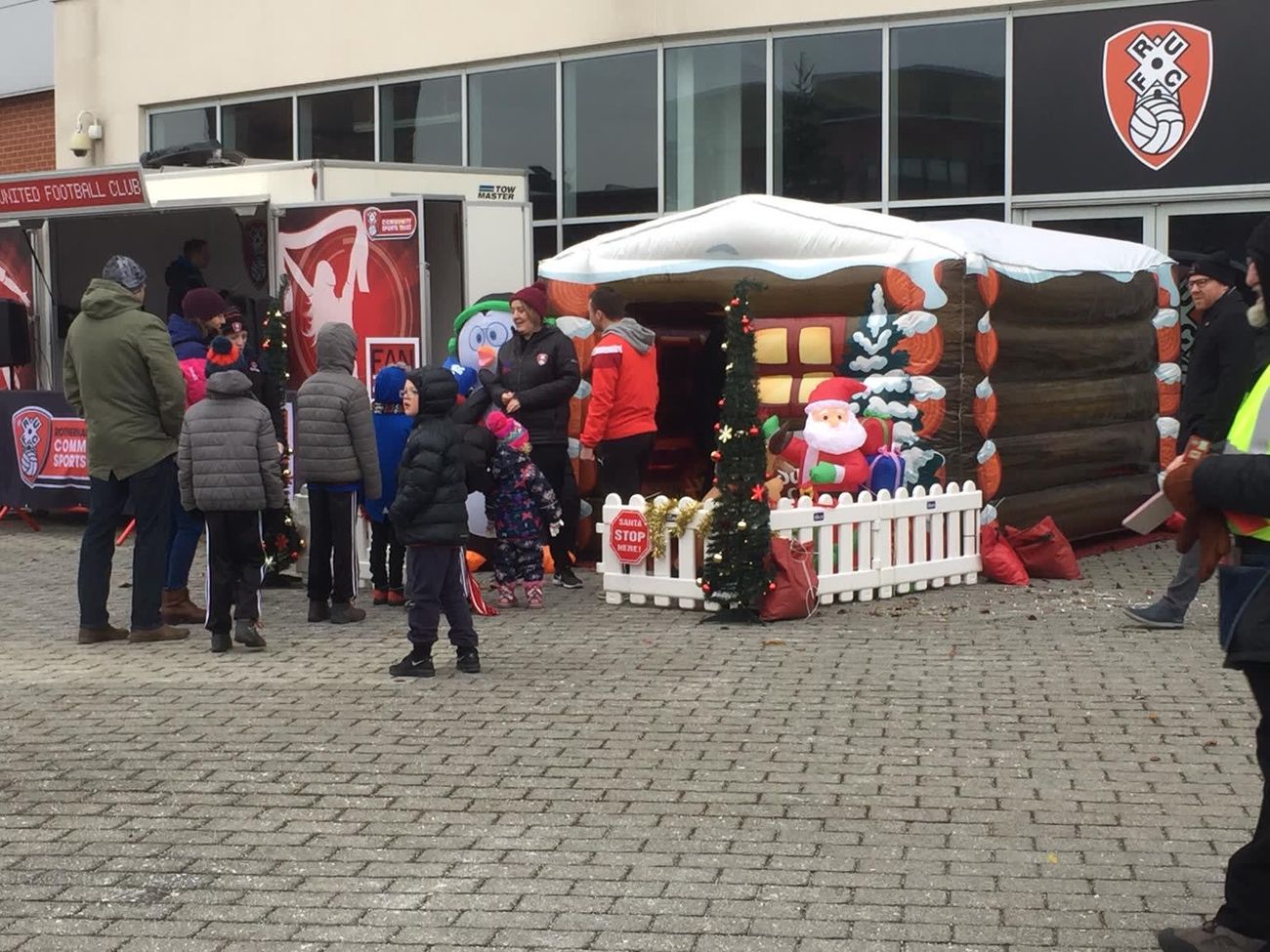 Santa's grotto set up outdoors at Rotherham United Football Club with inflatable Santa, picket fence and queue of families