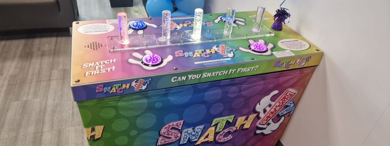 Snatch It rainbow-branded cabinet at an event venue alongside a balloon column