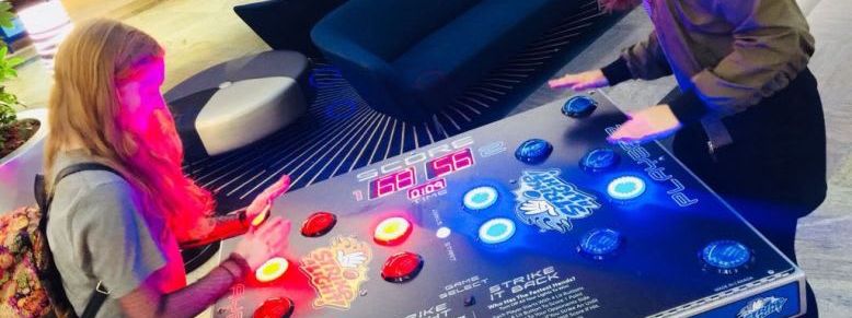 Two players competing head-to-head on the Strike a Light reaction table with red and blue illuminated dome buttons