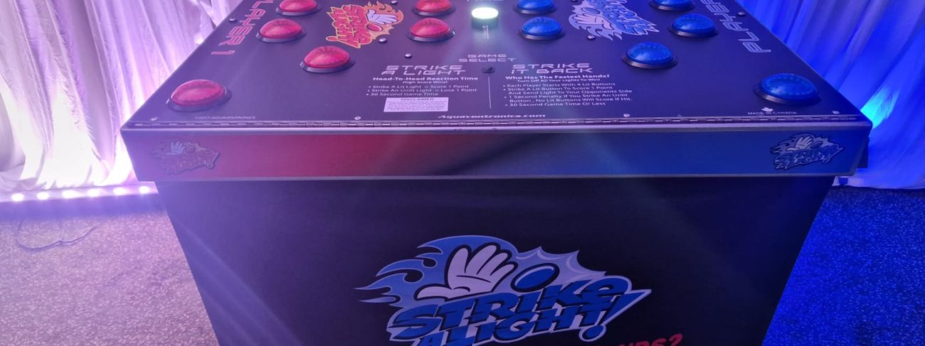 Strike a Light reaction table set up at an indoor evening event with red and blue neon buttons lit up, the branded skirt reading "How fast are your hands?"