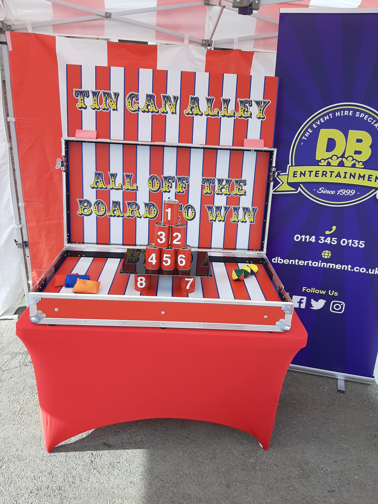 Red flight case open on its counter, with the striped backboard raised and eight numbered cans stacked on the shelf