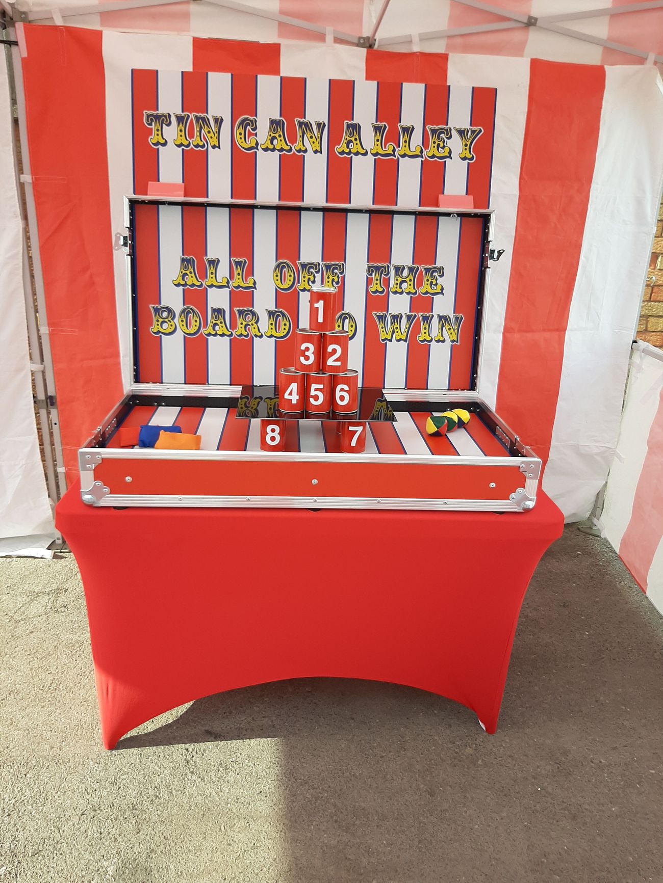 Numbered tin cans on the shelf with throwing balls and beanbags laid out on either side