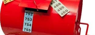 Close-up of a red metal tombola drum with wooden crank handle and numbered raffle tickets visible in the drawing slot