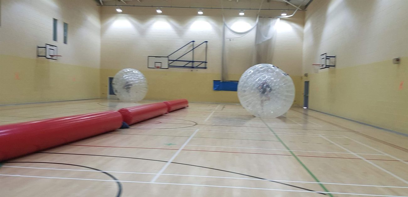 Two people running inside zorb balls on a sports hall floor