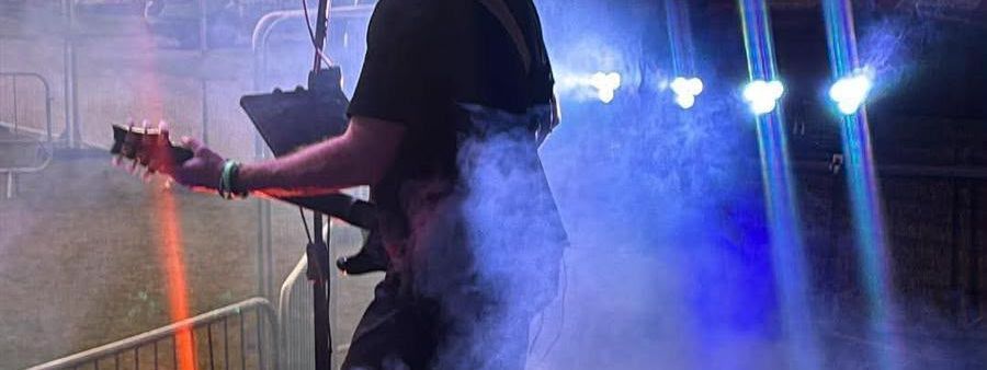 Guitarist silhouetted against a sunset on one of our stages, with stage haze and blue lighting